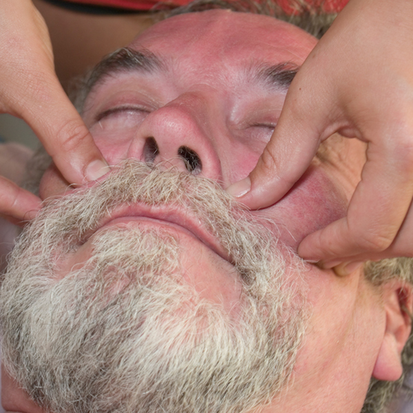 Man in his 50's on a massage table receiving facial massage.