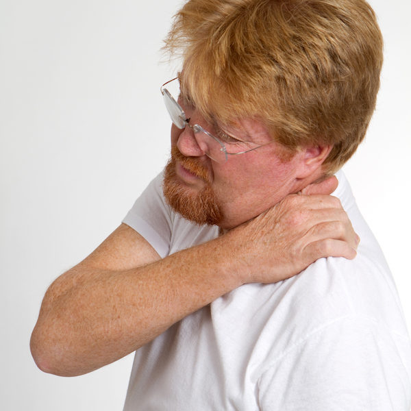 Mature man massages and squeezes his shoulder in pain.